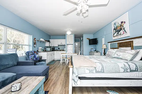 Turquoise-painted balcony/deck outside a house, with sliding glass doors, exposed beams, and blue bar-height chairs along a railing.