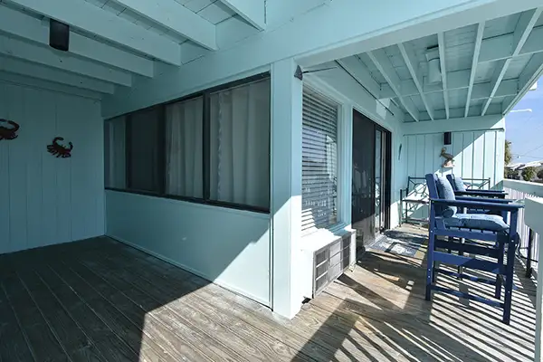 230-Oversized balcony overlooking the Beach - Ocean View Vacation Rentals Turquoise-painted balcony/deck outside a house, with sliding glass doors, exposed beams, and blue bar-height chairs along a railing.
